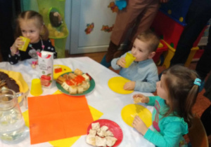 Dzieci siedzą przy stole i jedzą smakołyki