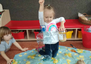 Dziewczynka kleczy i trzyma karmnik zrobiony z butli