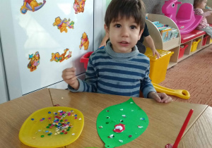 Chłopiec wykleja bombkę kolorowymi cekinami