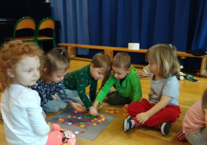Dzieci siedzą na podłodze i układają węża z kolorowych kawałków filcu
