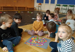 Dzieci siedzą na podłodze i układają węża z kolorowych kawałków filcu