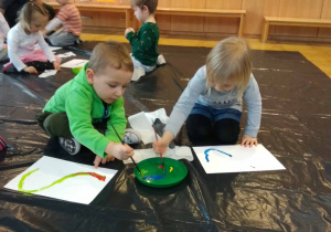 Dzieci siedzą na podłodze i malują farbami