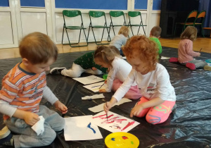 Dzieci siedzą na podłodze i malują farbami