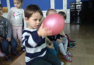 Dzieci siedzą na ławkach i słuchają, chłopiec ogląda balon