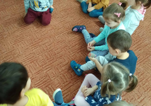Dzieci siedzą w półkolu i ogladaja i dotykaja wałki