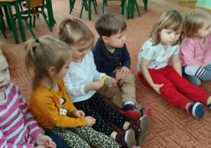 Dzieci siedzą w półkolu i ogladaja i dotykaja wałki