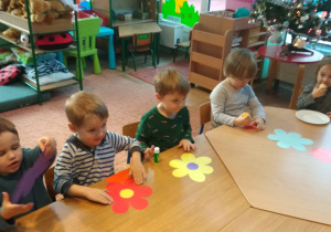 Dzieci siedzą przy stole i smarują sylwety kwiatów klejem