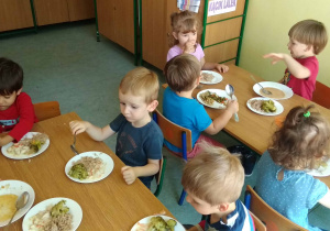 Dzieci siedza przy stołach i jedzą obiad