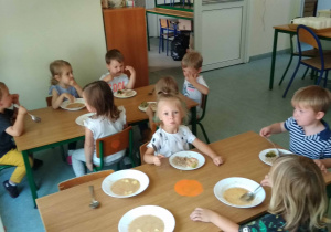 Dzieci siedza przy stołach i jedzą obiad