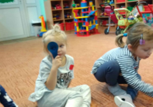 Dzieci siedzą w kole i przykładają kolorowe szkiełka do oczu