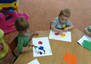 Dzieci siedzą przy stole i maluja farbami