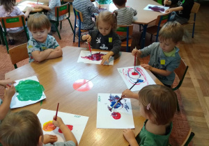 Dzieci siedzą przy stole i maluja farbami