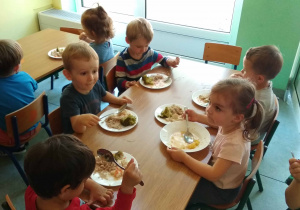 Dzieci siedza przy stole i jedzą obiad
