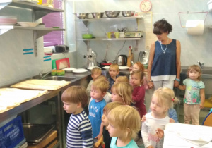 Dzieci stoją w kuchni i słuchają pani Kucharki która opowiada o swojej pracy