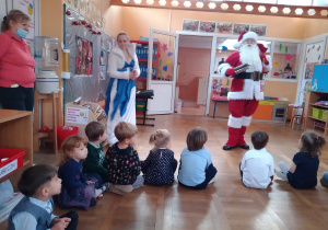 Dzieci siedzą na podłodze i rozmawiajają z Mikołajem