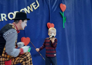 Clown wraz z chłopcem stoją na scenie, Clown prezentuje sztuczkę