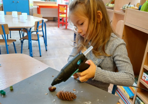 Dziewczynka łączy materiał przyrodniczy za pomoca pistoletu do kleju na gorąco