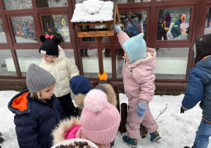Dzieci wsypują ziarna do karmnika