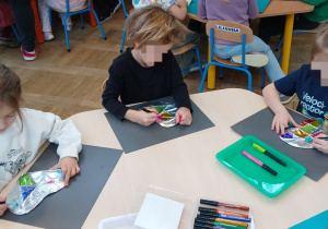 Dzieci siedząprzy stolikach i dekorują markerami serca