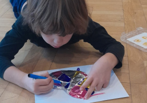 Chłopiec lezy na podlodze i koloruje markerem serce