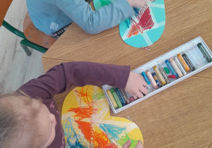 Dzieci siedzą przy stolikach i kolorują pastelami serca