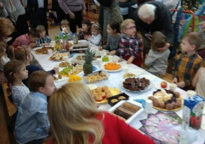 Dzieci wraz z dziadkami przy stole. Słodki poczęstunek dla dziadków i babć.